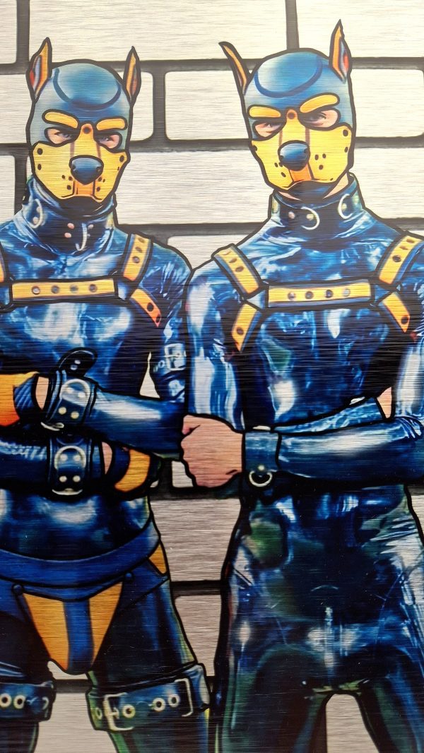 Détail de deux mecs en gear latex bleu et jaune, masques puppy et harnais, debout bras croisés sur fond de mur tagué.