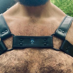 Mec de la meute, Harnais noir G.W.F porté sur un torse velu, vue frontale avec logo tête de loup visible, forêt en arrière-plan