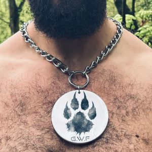 Collier à médaillon rond en céramique blanche avec patte de loup noire, porté sur torse velu.