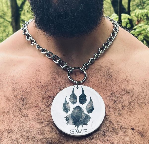 Collier à médaillon rond en céramique blanche avec patte de loup noire, porté sur torse velu.