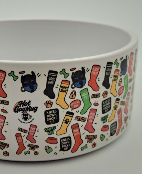 Gros plan sur la gamelle VILAIN PUPPY recouverte de motifs colorés inspirés du puppy play: chaussettes avec slogans (good boy, Pup Mode On, Sniff me...) têtes de puppys, os, cadenas, et logo Hot Gay Mug arc en ciel